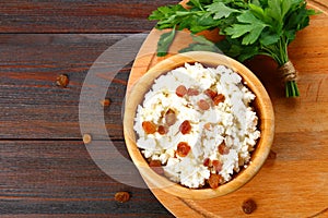 Homemade cottage cheese with almonds and raisins in a bowl on a wooden table.