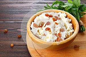 Homemade cottage cheese with almonds and raisins in a bowl on a wooden table.