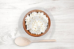 Homemade cottage cheese, curd in a bowl with spoon on a white rustic wooden table background. Healthy food.