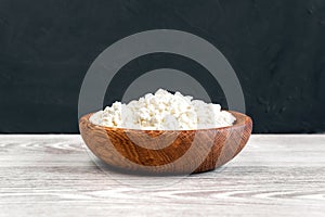 Homemade cottage cheese, curd in a bowl on a white rustic wooden table with black background.