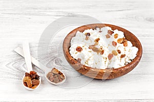 Homemade cottage cheese, curd with raisins in a bowl on a white rustic wooden table with black background. Healthy food.