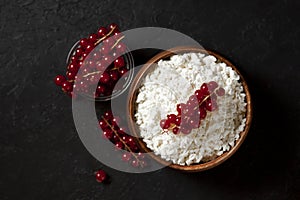 Homemade cottage cheese with currants in a wooden plate against a dark background, a healthy milk breakfast with berries