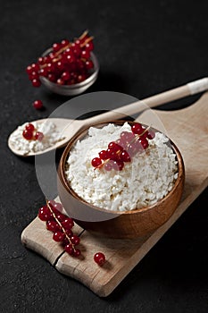 Homemade cottage cheese with currants in a wooden plate against a dark background, a healthy milk breakfast with berries on a
