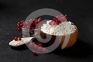 Homemade cottage cheese with currants in a wooden plate against a dark background, a healthy milk breakfast with berries on a