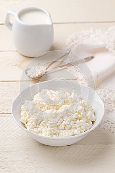 Homemade cottage cheese and jug of cream on a white wooden table