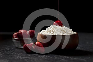 Homemade cottage cheese with strawberries and jam in a wooden plate against a dark background, adding red cream to a milk