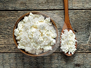 Homemade cottage cheese in a wooden bowl with a spoon on a rustic wooden table.