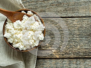 Homemade cottage cheese in a wooden bowl with a spoon on a rustic wooden table.
