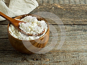 Homemade cottage cheese in a wooden bowl with a spoon on a rustic wooden table.