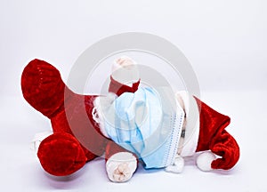 Homemade cotton Santa Claus lying or fallen play with a mask to protect against Covid-19 or Coronavirus photo