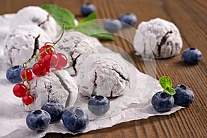 Homemade cracked cookies with powdered sugar on the baking paper near blueberries, red currant and peppermint leaves