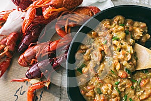 Homemade crawfish etouffee in a cast iron pan. Shown with whole boiled crawfish on a wood background.