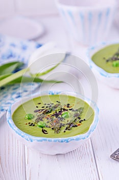 Homemade cream soup with asparagus and green peas on a white wooden background
