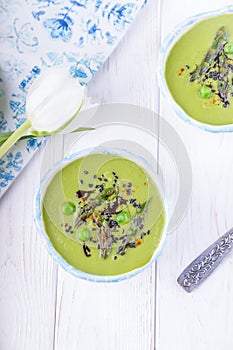 Homemade cream soup with asparagus and green peas on a white wooden background