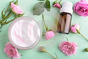 Homemade creame and essential oil with roses on wooden background