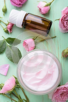 Homemade creame and essential oil with roses on wooden background