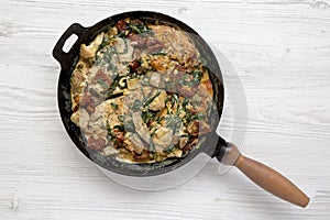 Homemade Creamy Tuscan Chicken in a cast iron pan on a white wooden background, top view. Flat lay, overhead, from above