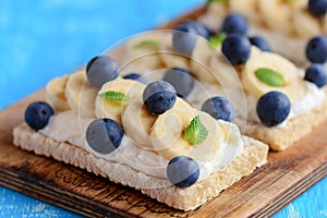 Homemade crispbread toast with cottage cheese, banana and berries on wooden board. Cottage cheese sandwich idea. Closeup