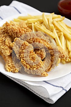 Homemade Crispy Chicken Tenders and French Fries on a white plate on a black background, low angle view. Close-up