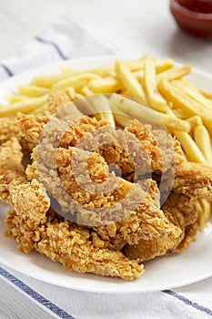 Homemade Crispy Chicken Tenders and French Fries on a white plate, side view. Close-up