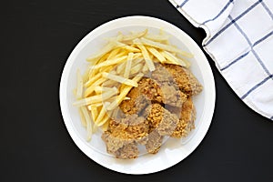Homemade Crispy Chicken Wings and French Fries on a white plate on a black background, top view. From above, overhead, flat lay