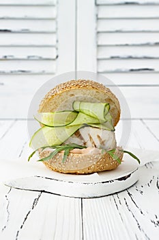 Homemade crispy spring fish burger with spicy chilli mayo on white rustic wooden board over light background. Copy space.