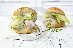 Homemade crispy spring fish burger with spicy chilli mayo on white rustic wooden board over light background. Copy space.