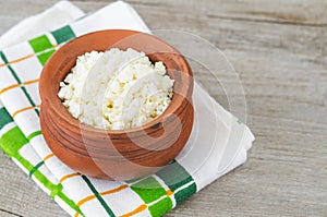 Homemade crumbly farmer\'s cheese in a clay pot. Wooden background. Copy space