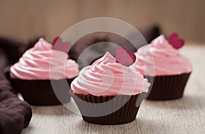 Homemade cupcakes traditional sweet dessert with pink cream and red hearts on vintage cloth background.