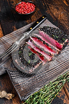 Homemade Cut Grilled Sesame Tuna steak on a cutting board. Dark Wooden background. Top view