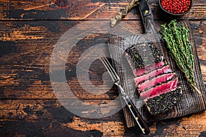 Homemade Cut Grilled Sesame Tuna steak on a cutting board. Dark Wooden background. Top view. Copy space