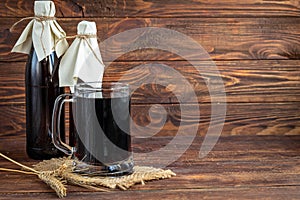 Homemade dark beer in bottles and a glass on a dark background. Nearby are barley grains and ears of wheat. Dark background