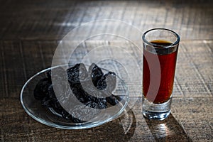 Homemade dark damson plum brandy in glasses on a wooden table, closeup. Drink from dry plums