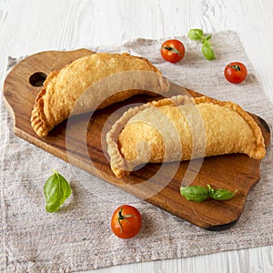 Homemade Deep Fried Italian Panzerotti Calzone on a rustic wooden board on a white wooden background, low angle view. Close-up