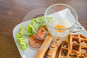 Homemade delicious american breakfast with soft-boiled egg, waffles, sausage, tomato, lettuce on white plate on wood table, top