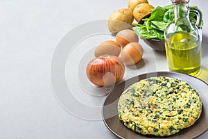 Homemade delicious potatoes eggs frittata with spinach on plate. Recipe ingredients onion olive oil in bottle on kitchen table