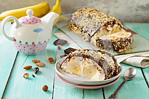 Homemade dessert with cream cheese, banana, chocolate icing and nuts on a rustic wooden table