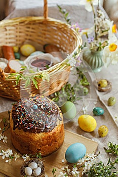 Homemade easter bread, natural dyed easter eggs, ham, beets, butter in basket on rustic table with spring blossoms and linen
