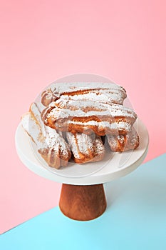 Homemade eclairs with powdered sugar. Cream puffs filled vanilla custard and dusted with icing on a bright background.