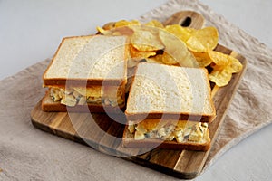 Homemade Egg Salad Sandwich with Potato Chips on a wooden board, side view