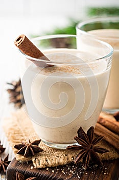 Homemade eggnog with grated nutmeg and cinnamon on white wooden table. Traditional Christmas drink.