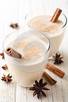 Homemade eggnog with grated nutmeg and cinnamon on white wooden table. Traditional Christmas drink.