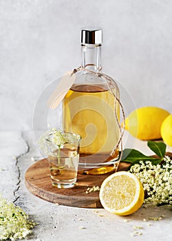 Homemade elderflower liquor in a bottle and glass summer drink with elder flower buds and lemon.