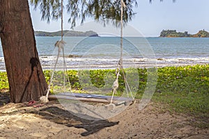 Homemade empty rope swing on a deserted beach against the background of the sea and blue sky with clouds.