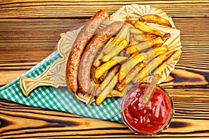 Homemade fast food, portion of french fries, ketchup, grilled sausages on wooden board.