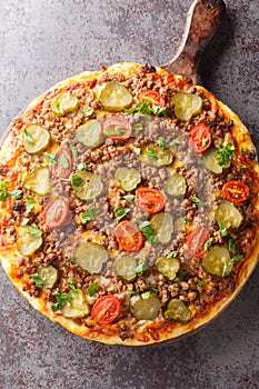 Homemade Fatty Hamburger Pizza with Beef Pickles and Tomato closeup on the wooden board. Vertical top view