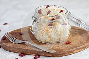 Homemade fermented sauerkraut with cranberries in a glass jar on a wooden stand and a fork next to it. Preparations, canning for