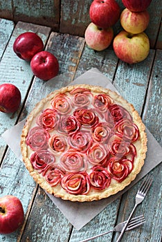 Homemade festive dessert. Tasty apple rose pie with cream filling served with organic apples on blue wooden background