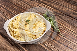 Homemade fettuccine with bechamel sauce in a white plate, rustic wooden table background, soft light - Italian food style