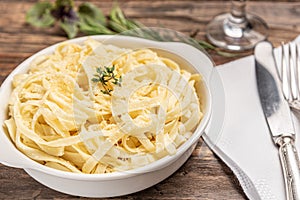 Homemade fettuccine with bechamel sauce in a white plate, rustic wooden table background, soft light - Italian food style